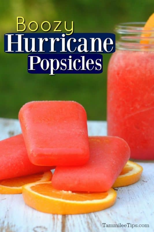 3 Boozy hurricane Popsicle sitting on oranges on a white background with a red drink in the background. 