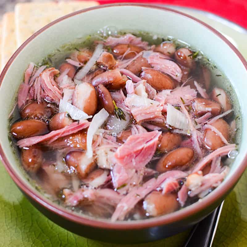 Ham and bean soup in a white bowl next to crackers on a green plate