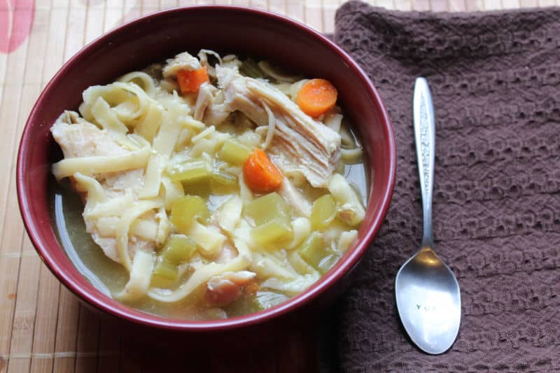 Crockpot Chicken Noodle Soup with a silver spoon on a brown placemat. 