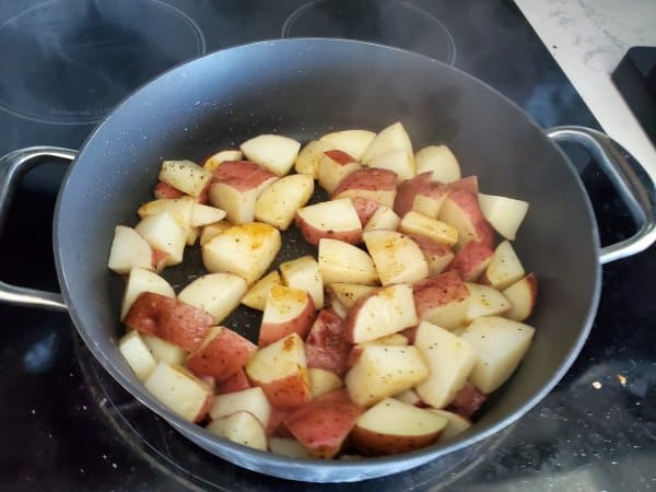 Red potatoes and seasoning in a dark skillet on the stove top
