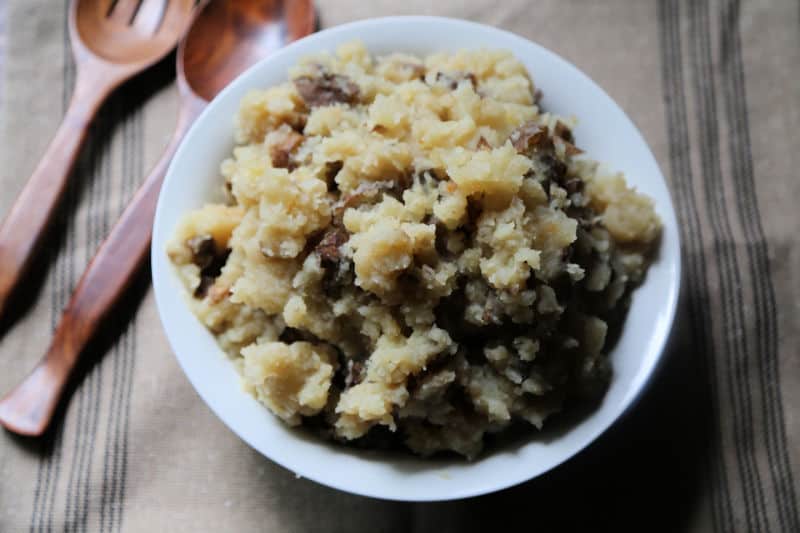 Crock Pot Garlic Mashed Potatoes in a white bowl on a tan placemat with 2 wooden spoons