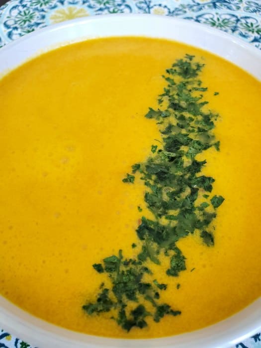 orange colored soup with a green leafy garnish in a white bowl on a colorful napkin