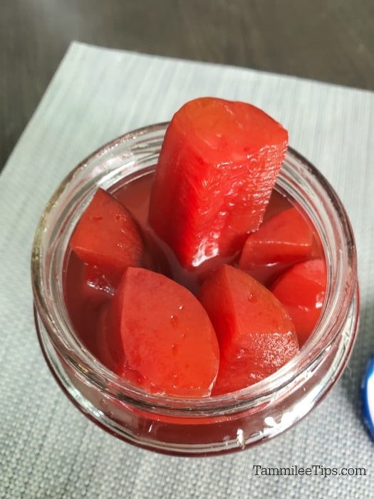 cherry kool aid pickles sticking out of a glass jar on a grey place mat 