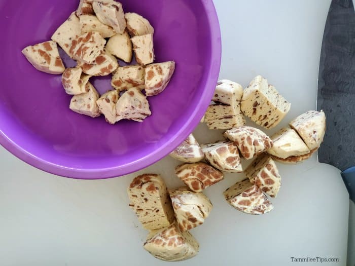 cut up refrigerated cinnamon rolls on a cutting board next to a purple bowl 