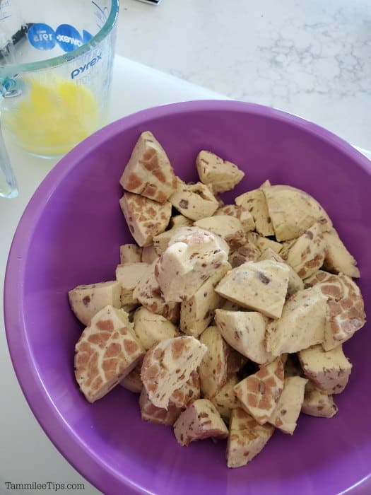 cinnamon roll pieces in a purple bowl next to melted butter in a measuring cup