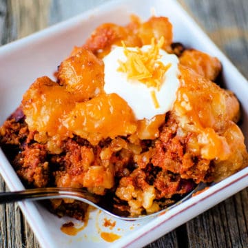 crockpot sloppy joe tater tot casserole in a white bowl topped with sour cream and cheddar cheese