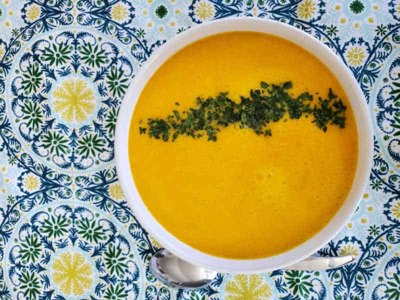 Carrot soup with a green garnish in a white bowl on a colorful napkin