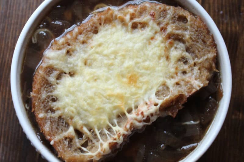 French onion soup in a white bowl with a slice of toast topped with melted cheese