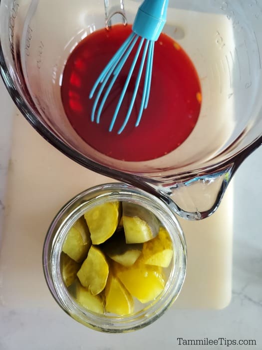 Cherry Kool Aid Pickles juice in a glass bowl and a jar of pickles