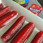 cherry kool aid pickles on a white platter with a jar of pickles and cherry kool aid packet