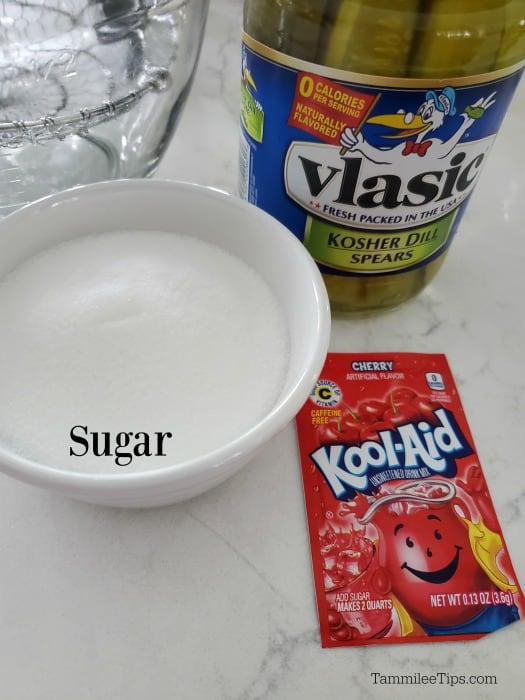 Kool Aid pIckles ingredients - pickles in a jar, sugar in a white bowl and cherry kool aid packet 