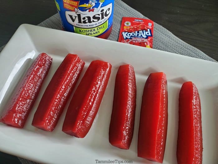 Kool Aid Pickles on a white platter next to a jar of pickles and a Cherry Kool Aid packet
