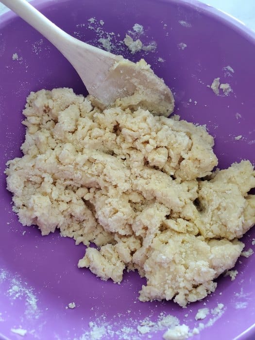 dough crumble in a purple bowl with a wooden spoon