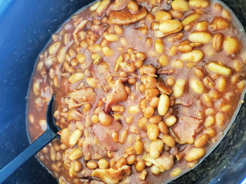 Baked beans and bacon in a slow cooker bowl with a spoon