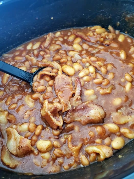 baked beans and bacon in a slow cooker bowl with a large spoon