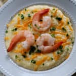 Crockpot Shrimp and Grits in a white bowl with green onion and cheddar cheese garnish