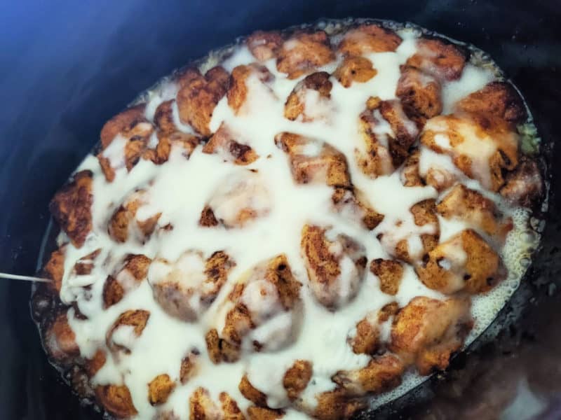 cinnamon roll monkey bread in the crock pot covered in icing