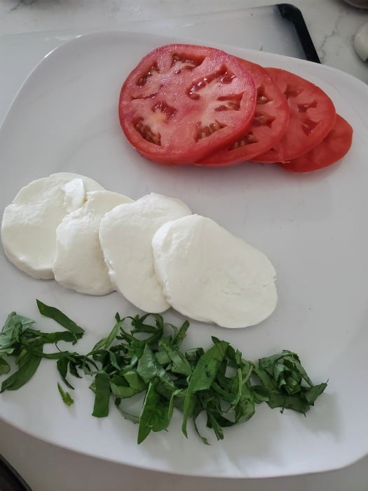 tomato slices, mozzarella cheese, and basil on a white plate