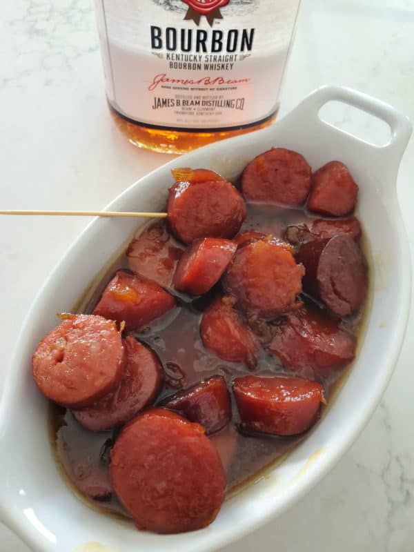 Sliced bourbon in a glaze sauce in a white bowl next to a bottle of bourbon