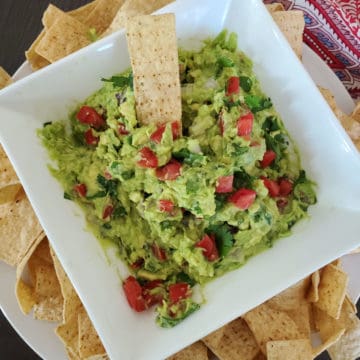 Guacamole with diced tomatoes in a white bowl with tortilla chips