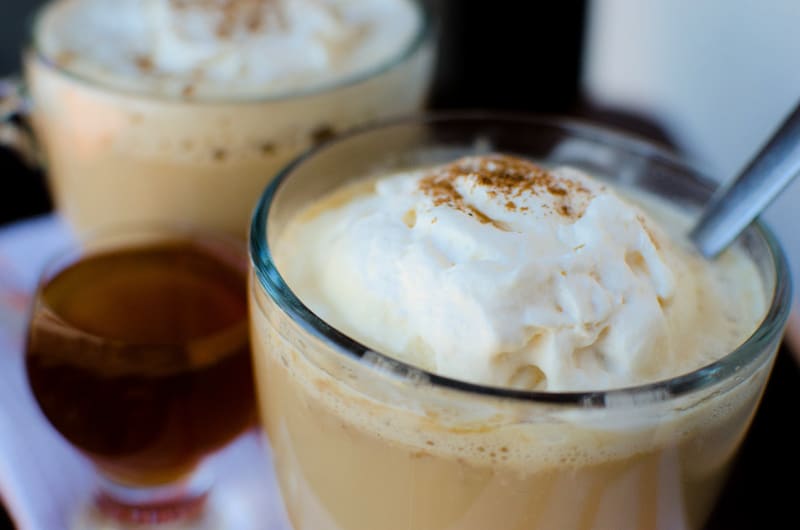 close up photo of a crockpot pumpkin spice latte in a clear glass mug with whipped cream. 