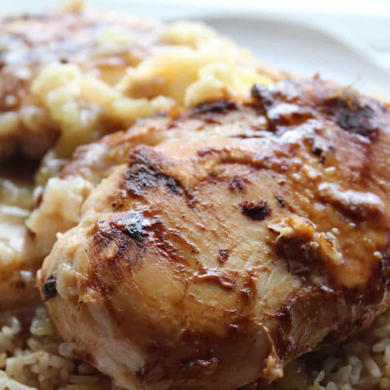 Hawaiian chicken breast next to rice and pineapples on a white plate