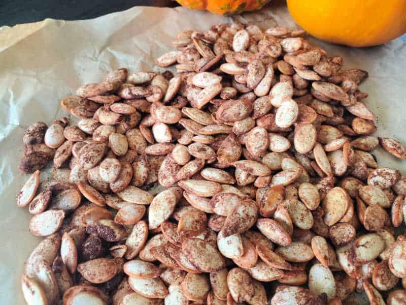 pumpkin spice pumpkin seeds on parchment paper with 2 pumpkins