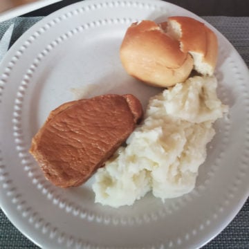 white plate with a roll, potatoes, and pork loin