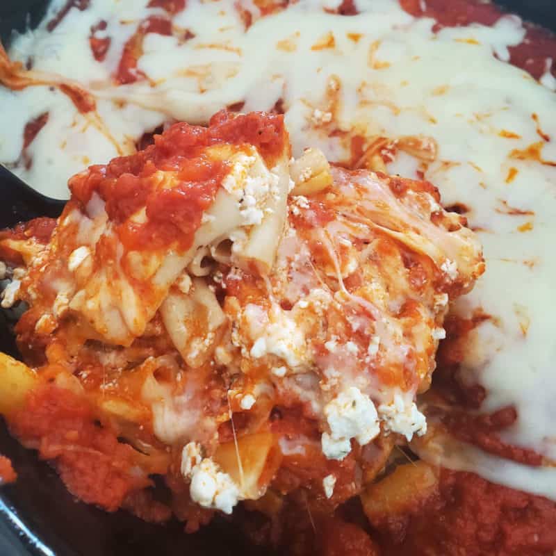cheesy baked ziti on a spoon lifting out of a slow cooker