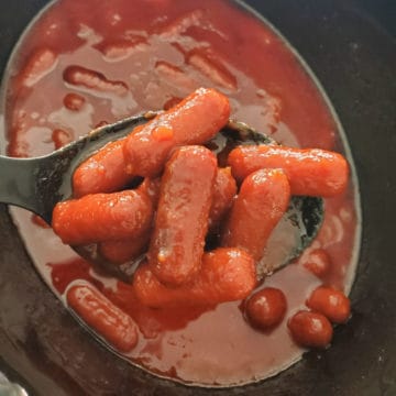 Crockpot Bourbon Little Smokies on a spoon lifting out of the slow cooker