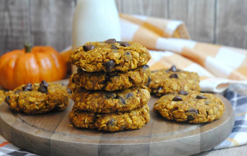 Stack of Pumpkin oatmeal cookies on a wooden board next to a pumpkin and glass of milk 