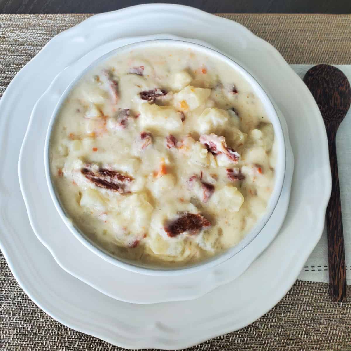 Ham and potato soup in a white bowl on a white plate with a wood spoon