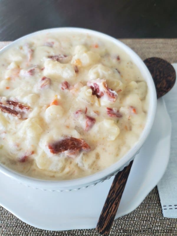 creamy ham and potato soup in a white bowl with a wooden spoon next to it