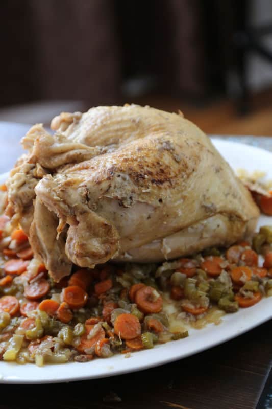 crock pot turkey on a white serving platter with carrots, celery, and onions cooked under it. 