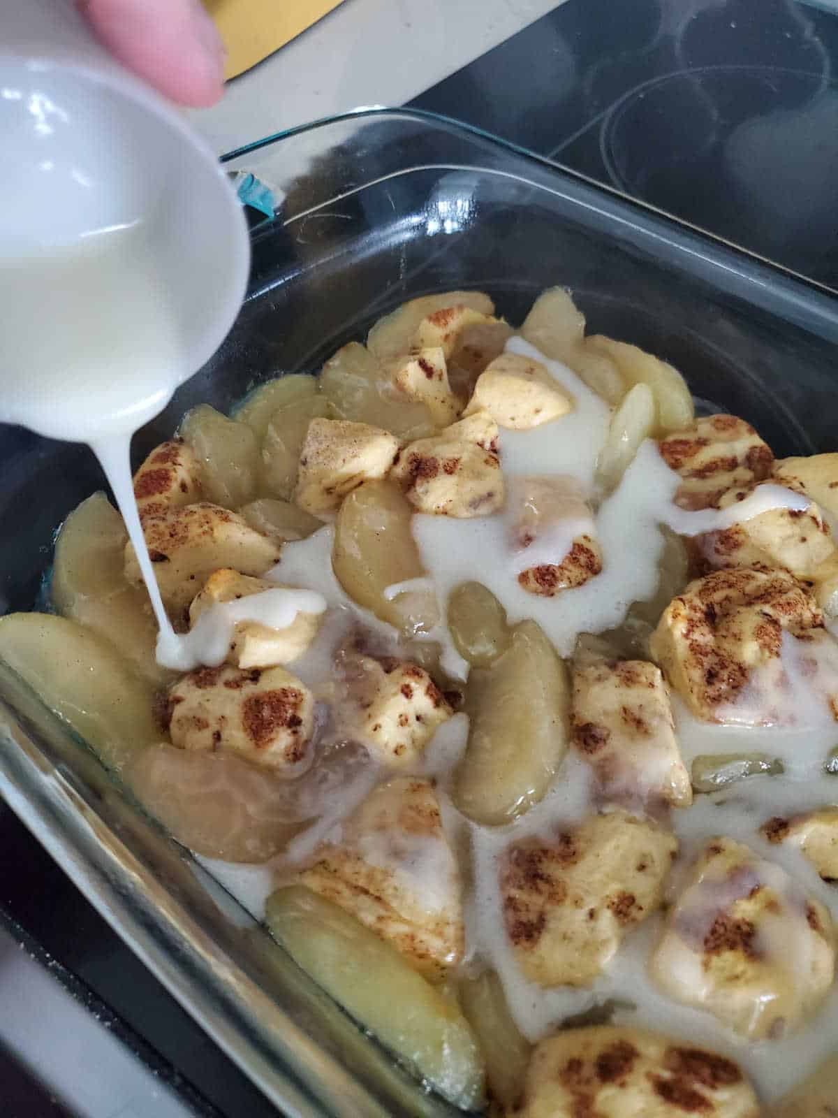 icing pouring over cinnamon roll and apple pieces