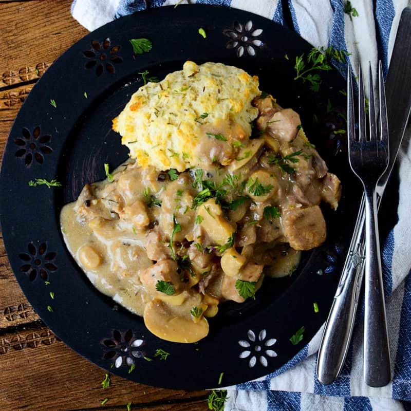 rosemary pork chop with cream sauce on a blue plate next to a fork and knife