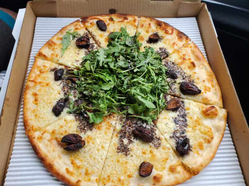 figs, arugula, and cheese on a pizza in a cardboard delivery box