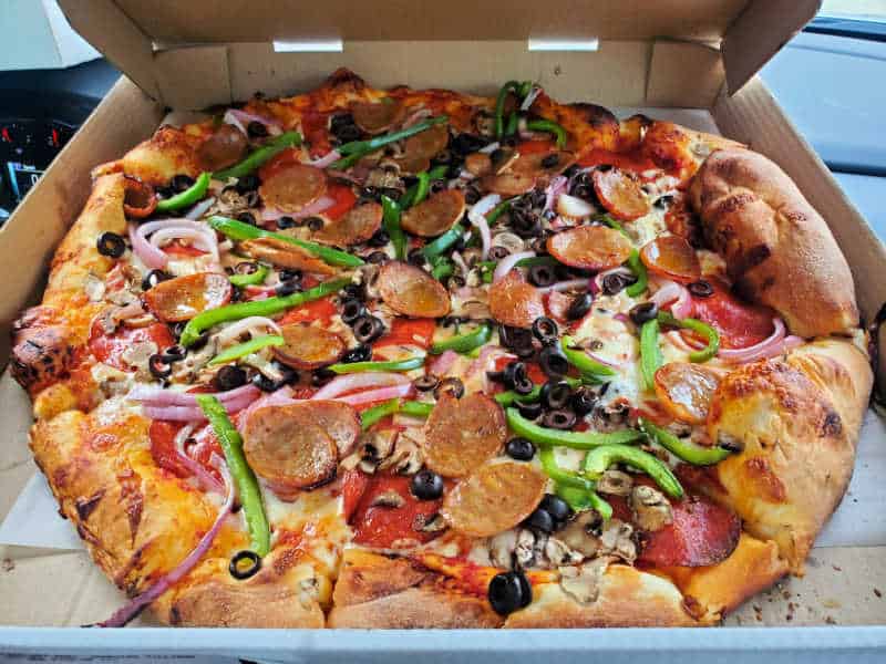 Pizza in a box with mushrooms, olives, peppers, pepperoni, and onions
