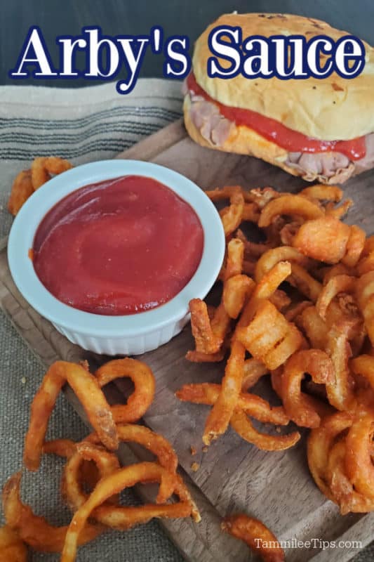 Arby's Sauce over a ramekin with red sauce on a wooden cutting board with curly fries and an Arby's Roast Beef Sandwich. 