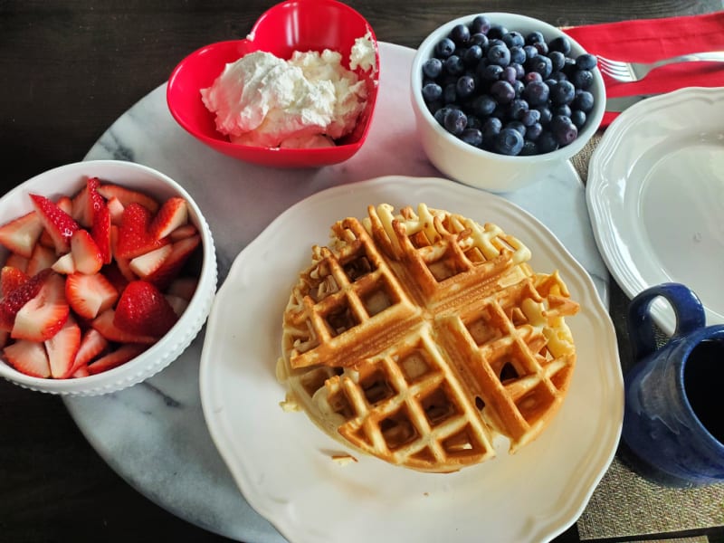 Bisquick Waffle on a white plate next to bowls of strawberries, whipped cream, and blueberries