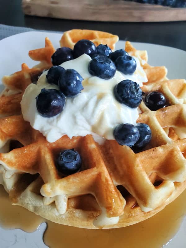 Bisquick waffle with whipped cream, blueberries, ands syrup on a white plate