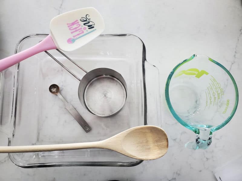 Spatula, wooden spoon, measuring tools, glass baking dish, and measuring cup on a white counter. 