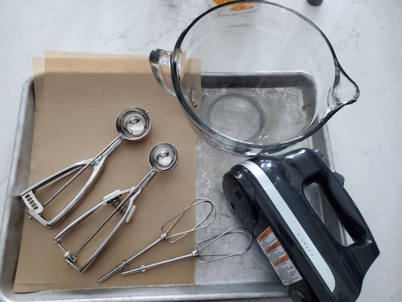 Cookie scoops, hand held mixer, glass batter bowl, parchment paper, and baking sheets