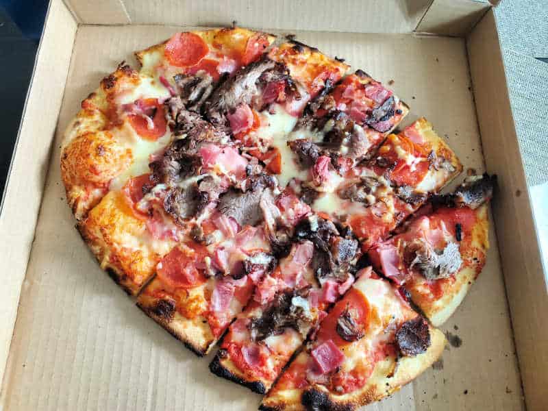 pepperoni, bacon, and prime rib on a pizza in a delivery box