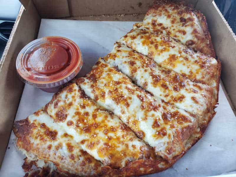 cheese bread next to a container of red sauce in a delivery box