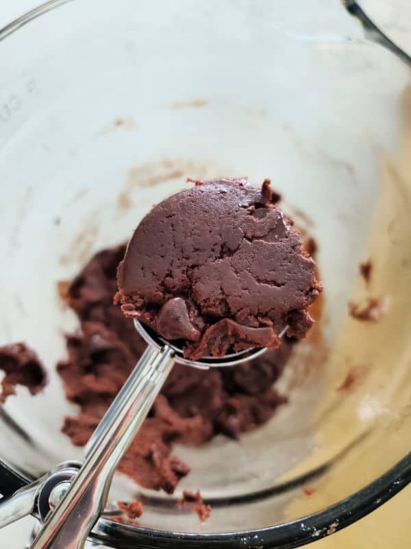 Cookie scoop with chocolate cookie dough held over a glass mixing bowl 