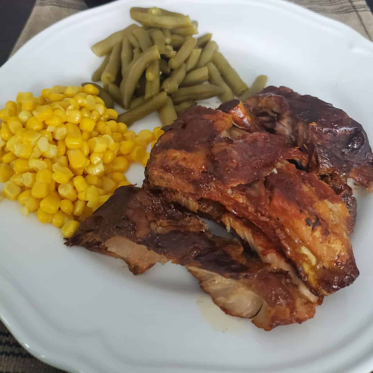dr pepper ribs next to corn and green beans on a white plate