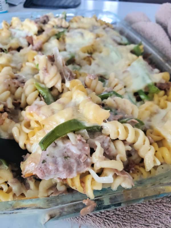 spoon scooping Philly cheesesteak casserole out of a glass baking dish