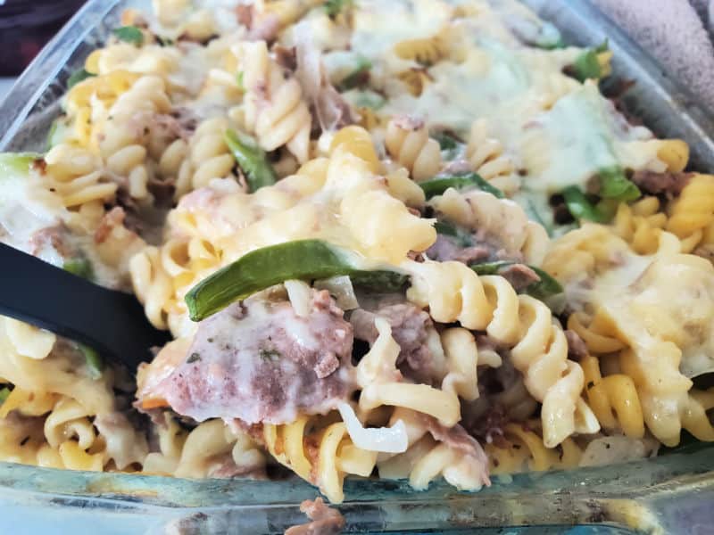 spoon lifting Philly Cheesesteak casserole out of a glass baking dish. 