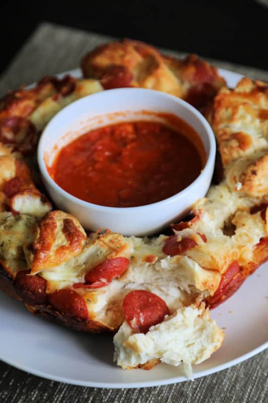 Pepperoni Pizza Monkey Bread on a white circle plate with marinara sauce in a bowl